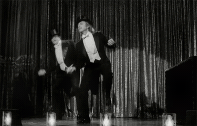 Two Men In Tuxedos Dancing On Stage GIF