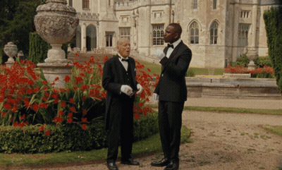 Two Men In Tuxedos Standing In Front Of A Large Building GIF