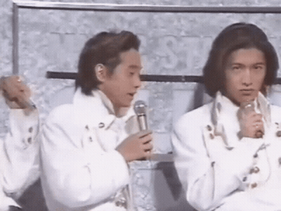 Two Men In White Jackets Are Sitting Next To Each Other And Holding Microphones . GIF