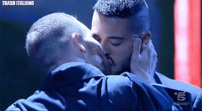 Two Men Kissing in Front of Mediaset Sign