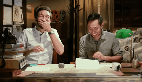 Two Men Laughing At Desk One Covering Mouth GIF