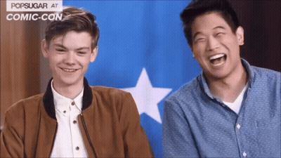 Two Men Laughing In Front Of Blue And White Popsugar Flag At Comic Con GIF