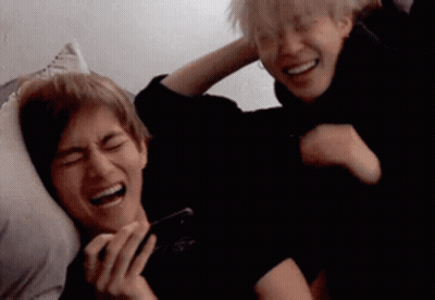 Two Men Laughing On Bed One Holding Phone GIF