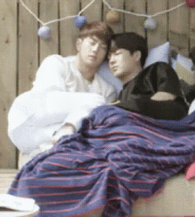 Two Men Laying On Bed With Striped Blanket GIF