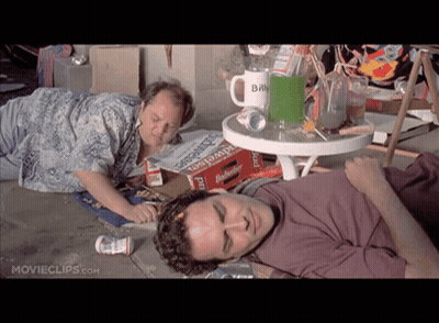 Two Men Laying On The Ground In Front Of A Table With A Mug That Says Billy GIF