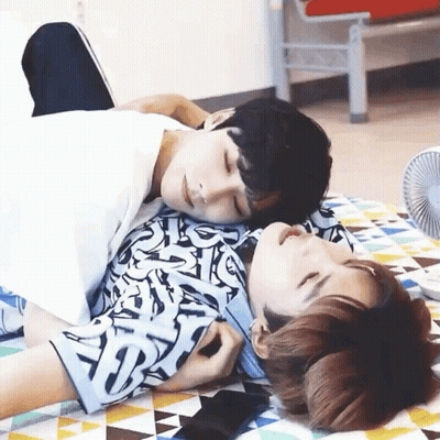 Two Men Laying on Top of Each Other on Blanket With Fan
