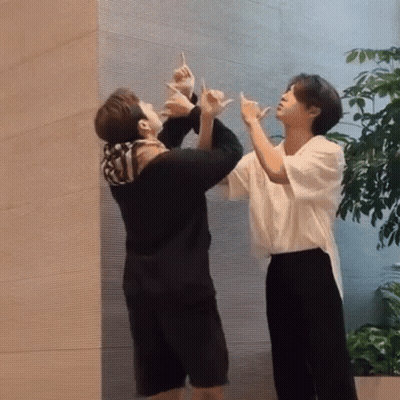 Two Men Making Hand Signs In Front Of Wall GIF