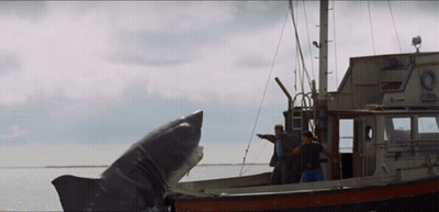 Two Men On A Boat With A Shark Coming Out Of The Water GIF