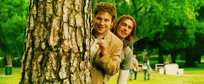 Two Men Peeking Behind Tree In Park GIF