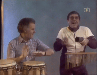 Two Men Playing Drums In Front Of BBC TV Screen GIF