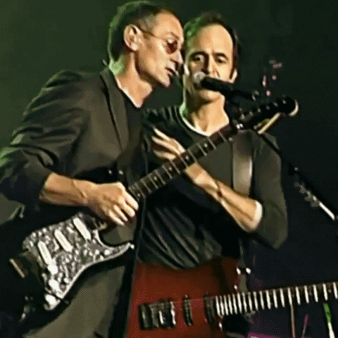 Two Men Playing Guitars And Singing Into Microphones GIF