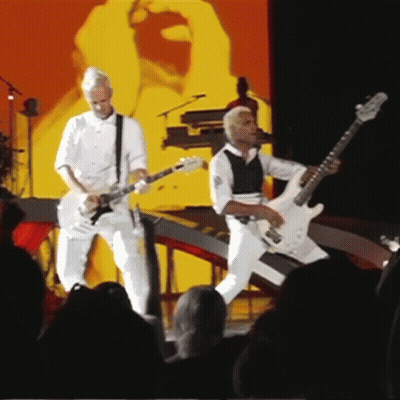 Two Men Playing Guitars On Stage GIF