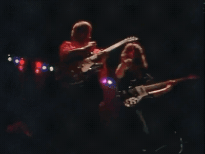 Two Men Playing Guitars On Stage With 'A' Shirt