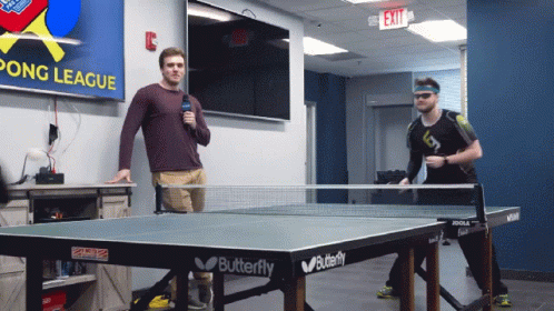 Two Men Playing Ping Pong In Front Of A Pong League Sign GIF