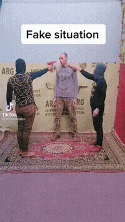 Two Men Pointing at Man on Rug in Front of Fake Situation Sign