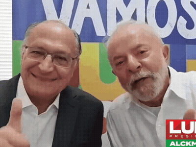 Two Men Posing In Front Of Vamos Sign GIF