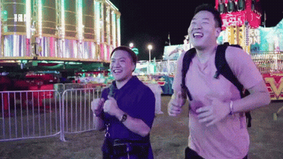Two Men Running And Laughing Near Carnival Ride GIF
