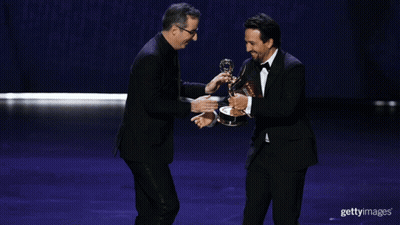Two Men Shaking Hands On A Stage While One Holds A Trophy GIF