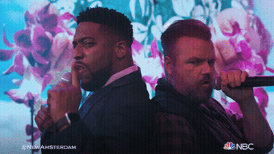 Two Men Singing In Front Of Floral Background With NBC Logo GIF