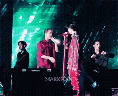 Two Men Singing Into Microphones On Stage With Green Light GIF