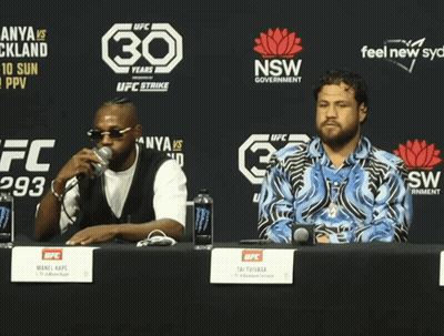 Two Men Sit At A Table In Front Of A Sign That Says 30 GIF