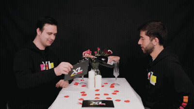 Two Men Sit At A Table With A Card That Says Xl GIF