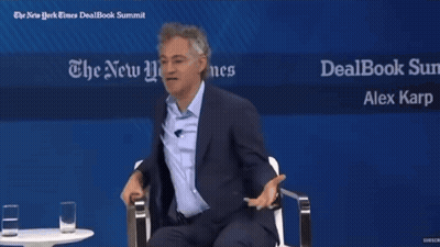 Two Men Sit In Front Of A Sign That Says Dealbook Summit GIF