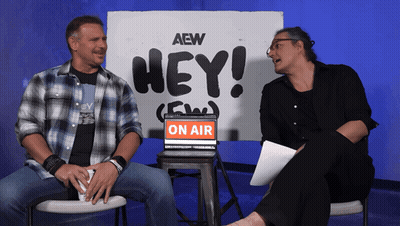 Two Men Sit In Front Of A Sign That Says Hey On Air GIF