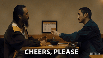 Two Men Sitting At A Table With Cheers Please Written On The Bottom Right GIF