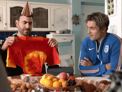 Two Men Sitting At A Table With One Wearing A Nike Jacket GIF