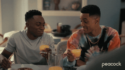 Two Men Sitting At A Table With Peacock Written On The Bottom Left GIF