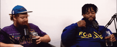 Two Men Sitting At Microphones One In Fog Hoodie GIF