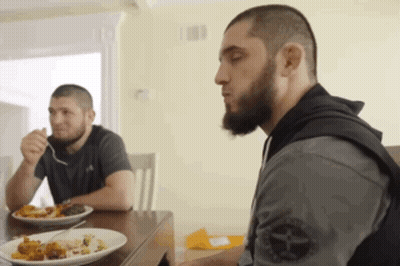 Two Men Sitting At Table Eating Food One With Beard GIF