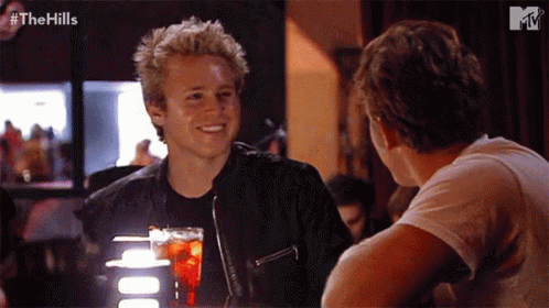 Two Men Sitting At Table With Drink GIF