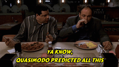Two Men Sitting At Table With Food And Quasimodo Sign GIF