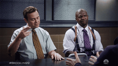 Two Men Sitting At Table With NBC GIF