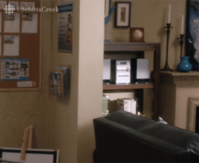 Two Men Sitting At Table With Schitt's Creek Sign GIF