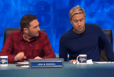 Two Men Sitting At Table With Sign Saying Jon And Russell GIF