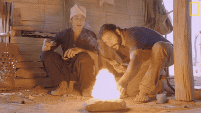 Two Men Sitting By Fire With National Geographic Logo GIF