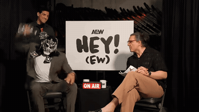 Two Men Sitting By Sign Saying Hey GIF