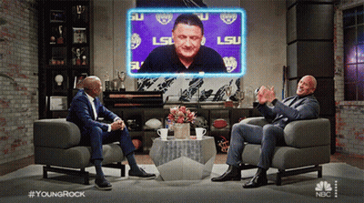 Two Men Sitting In Chairs Before LSU Screen GIF