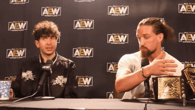 Two Men Sitting In Front Of A Wall That Says Aew Wrestling GIF