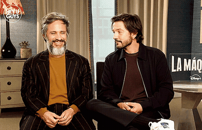 Two Men Sitting In Front Of La Mano Sign GIF
