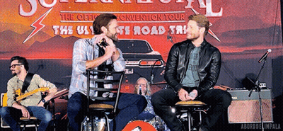 Two Men Sitting In Front Of The Ultimate Road Trip Sign GIF