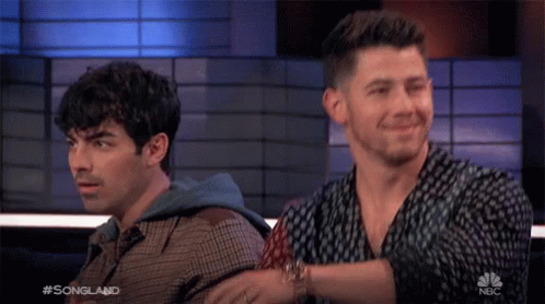 Two Men Sitting Next To Each Other On A Nbc Show GIF