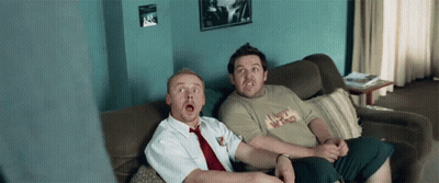 Two Men Sitting On A Couch One Of Whom Is Wearing A Shirt That Says I Bet Who GIF