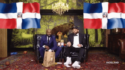 Two Men Sitting On A Couch With A Bag That Says City Market GIF