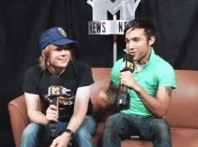 Two Men Sitting On A Couch With Microphones In Front Of A Sign That Says News GIF