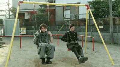 Two Men Sitting On A Swing Set In A Park GIF