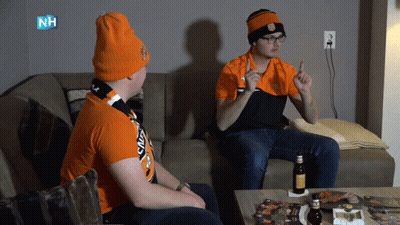 Two Men Sitting On Couch One With NH Logo Shirt GIF